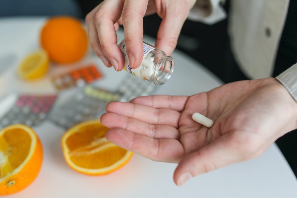 A white capsule in a person’s hand, with fruits and several sets of tablets in the background