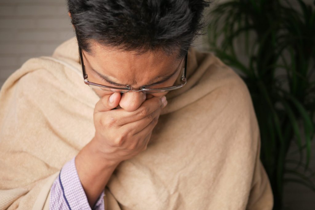 A man coughing while covered with a blanket