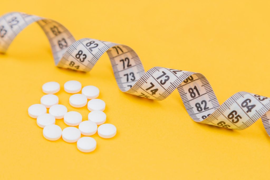 White tablets next to a measuring tape