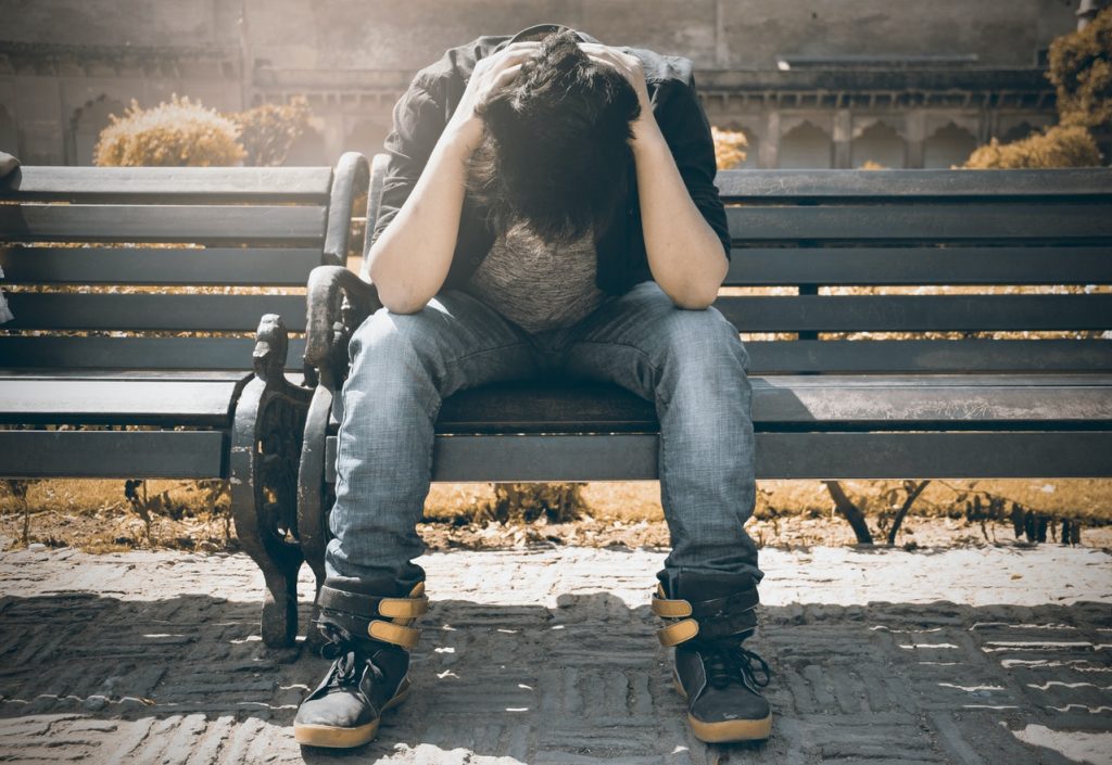 man sitting on bench with head in hands