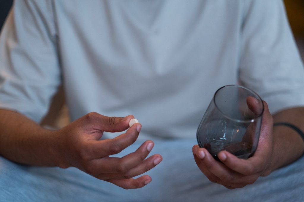 Person self-medicating, holding pill and glass