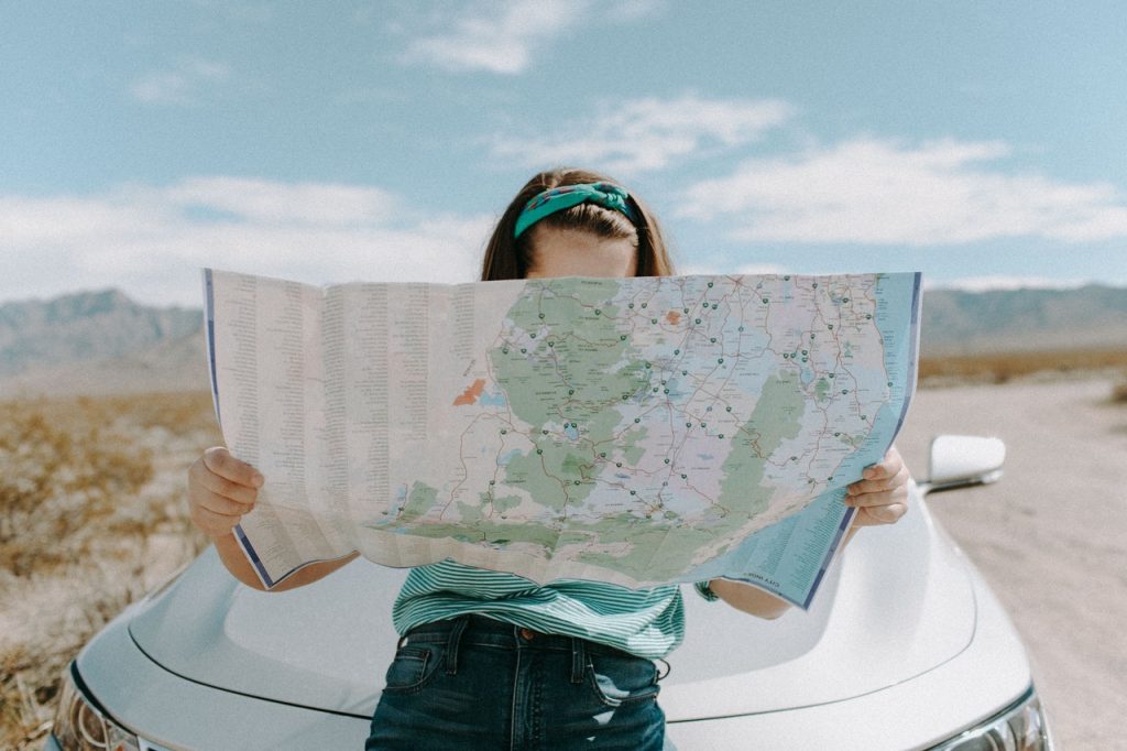 Woman holding map on road trip while sitting on the hood of a car