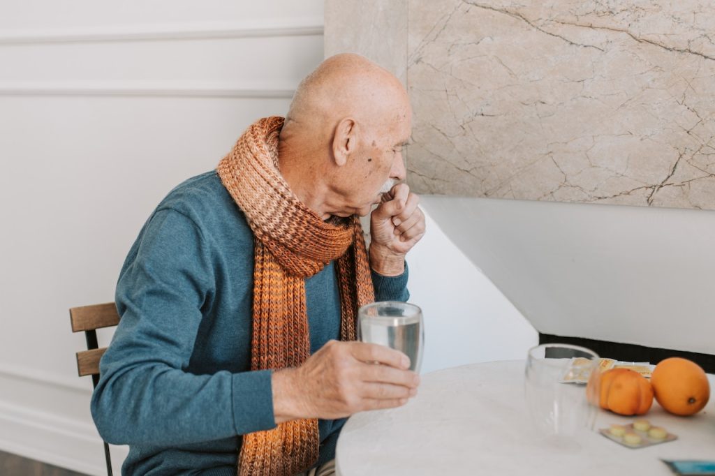 man coughing and holding a glass of water