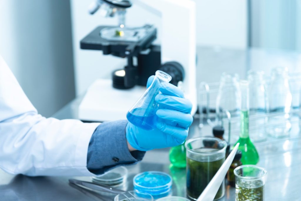 A scientist holding a beaker with blue liquid in a laboratory