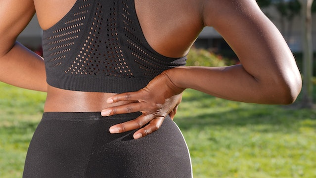 woman with lower back pain rubbing her back